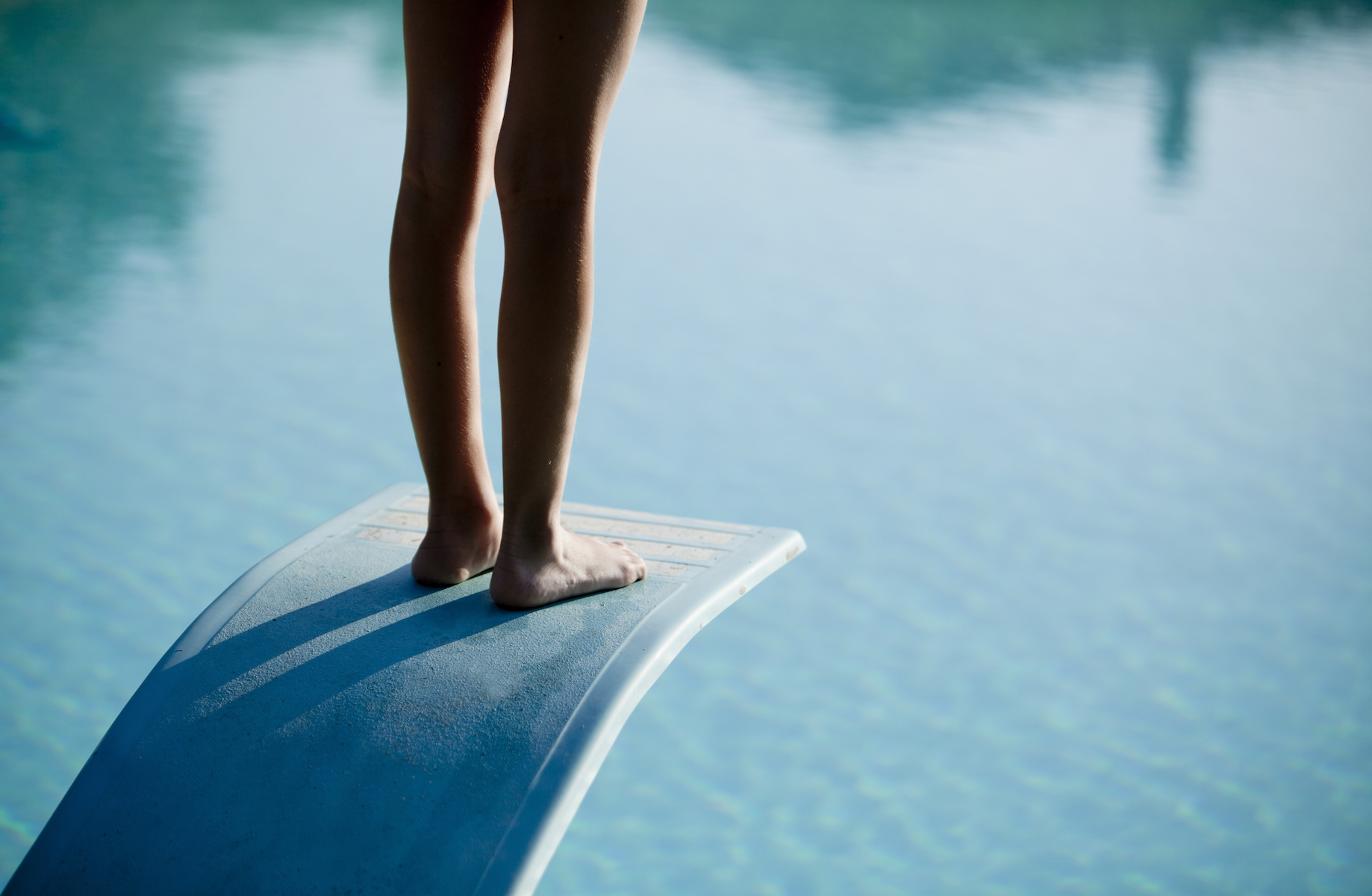 Shot of bare legs on diving board above blue water